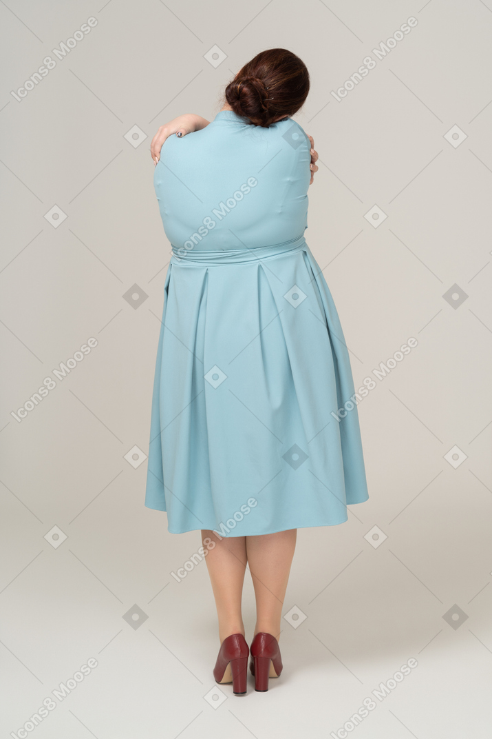 Женщина в синем платье обнимает себя, вид сзади