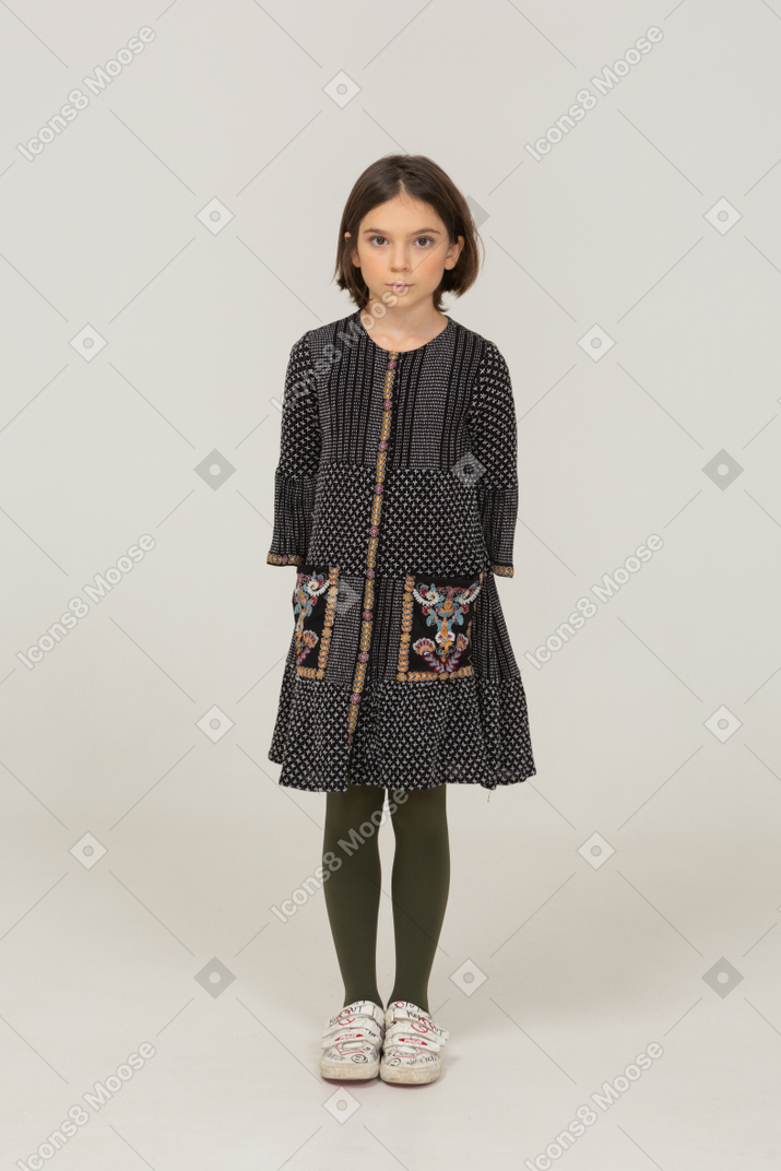 Vista frontale di una bambina in abito che guarda la telecamera tenendosi per mano dietro