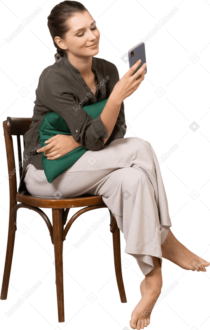 Vista frontal de una mujer joven sonriente sentada en una silla mientras revisa su teléfono