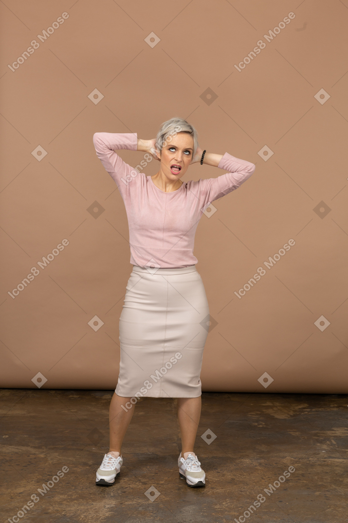 Vista frontal de uma mulher com roupas casuais em pé com as mãos atrás da cabeça