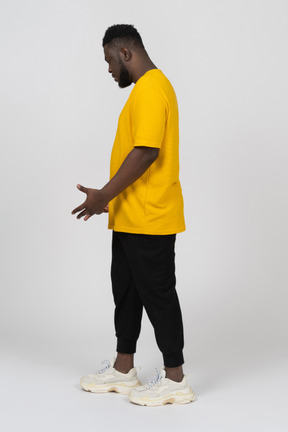 Vista lateral de um jovem homem de pele escura gesticulando pensativo em uma camiseta amarela