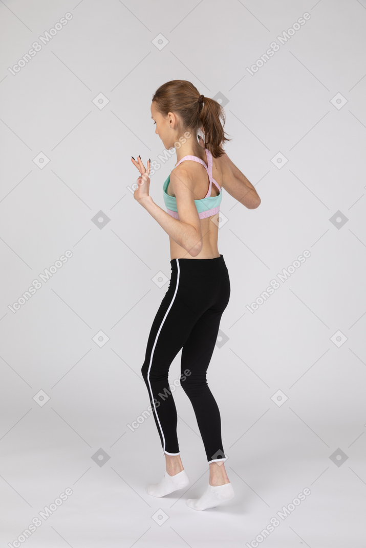 Three-quarter back view of a teen girl in sportswear walking cautiously on her tiptoes