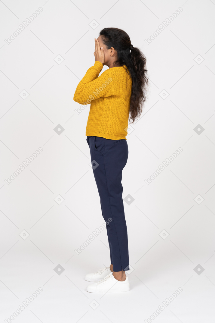 Vista lateral de una niña en ropa casual que cubre la cara con las manos