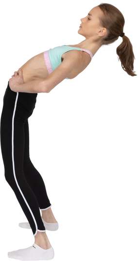 Vue latérale d'une adolescente en tenue de sport mettant les mains sur les hanches en se penchant en arrière