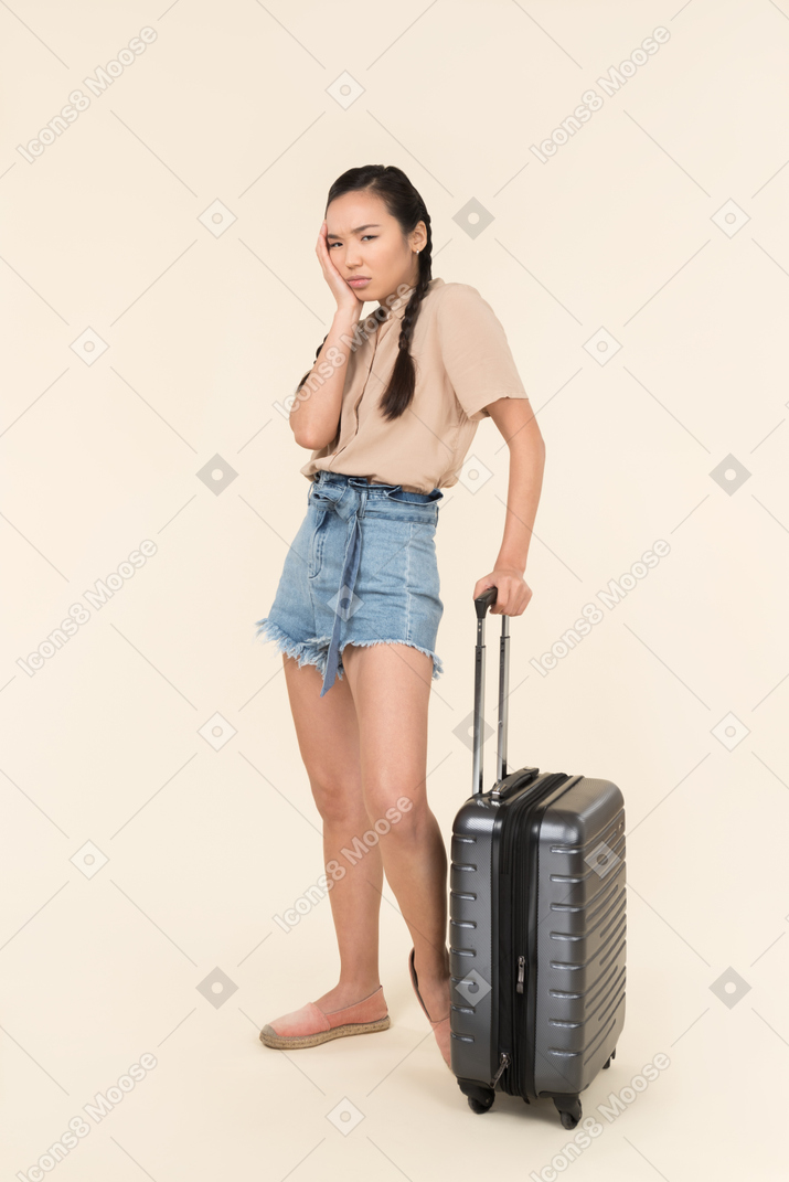 Sad looking young female traveller standing near suitcase