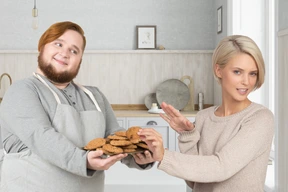 A man in an apron offering cookies to a woman