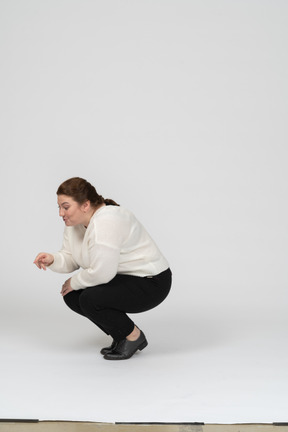 Vista laterale di una donna grassoccia in abiti casual accovacciata