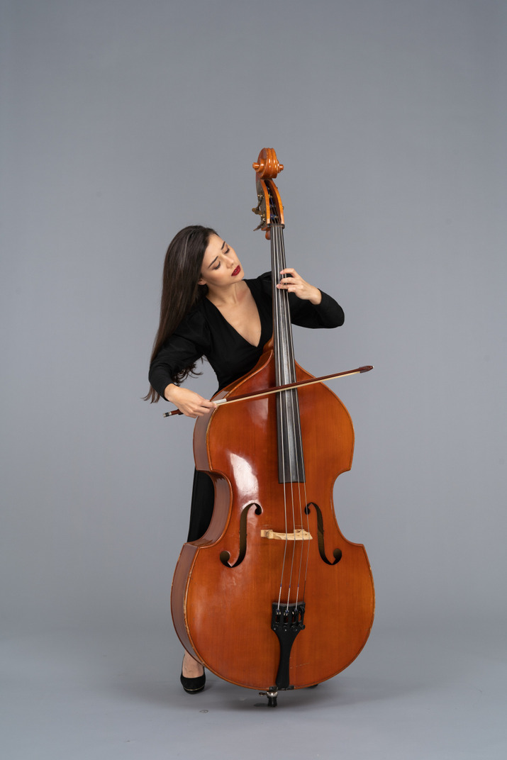 Front view of a young woman in black dress playing the double-bass with a bow while looking aside