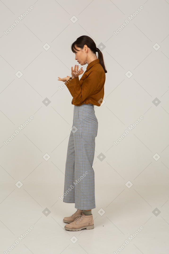 一位身着马裤和上衣的质疑亚洲年轻女性举手的侧视图