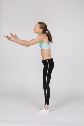 Vista lateral de una jovencita en ropa deportiva en cuclillas y poniendo las manos en las caderas
