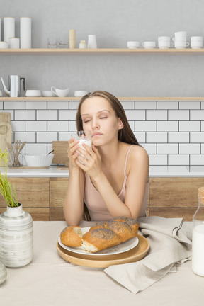 A woman holding a cup of milk and sitting at a table with bakery on a plate