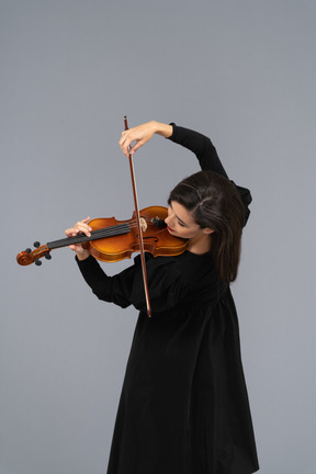 Close-up de uma jovem alegre de vestido preto tocando violino