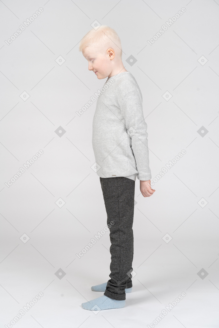 一个小男孩背着他的手站着的侧视图
