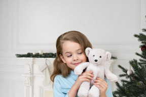 Little girl telling her toy bear to make a wish under a christmas tree