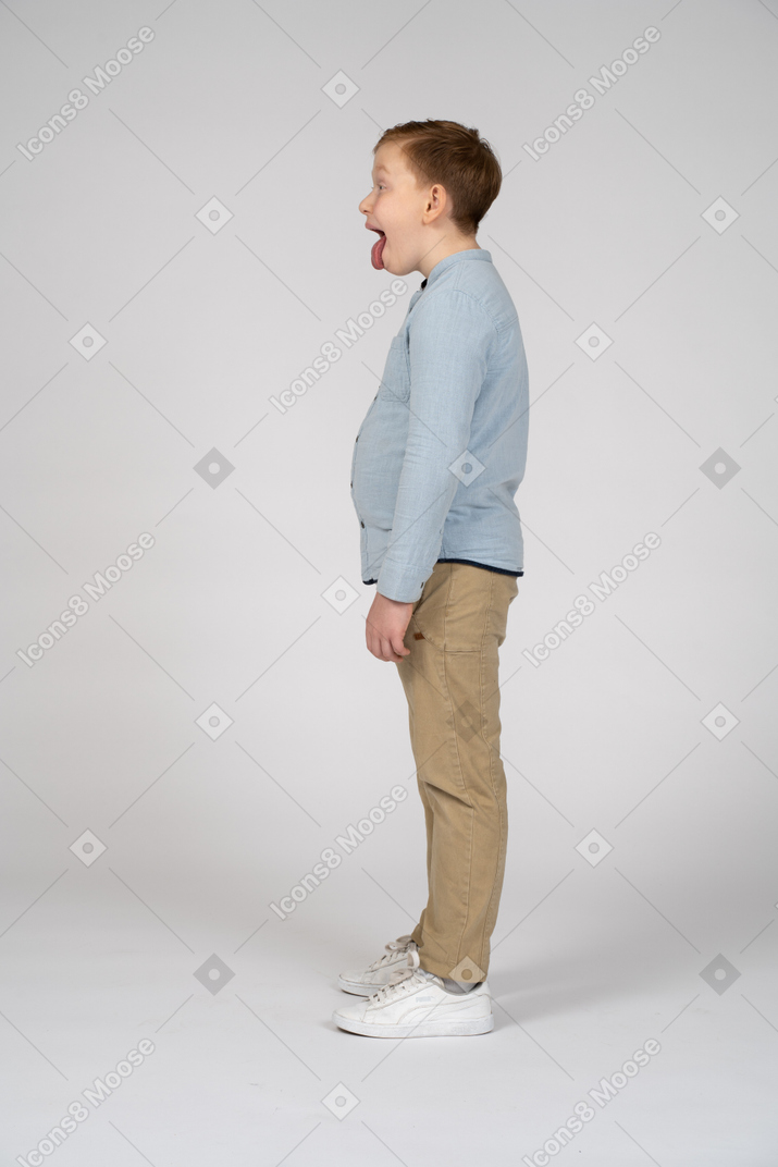 Side view of a cute boy in casual clothes showing tongue