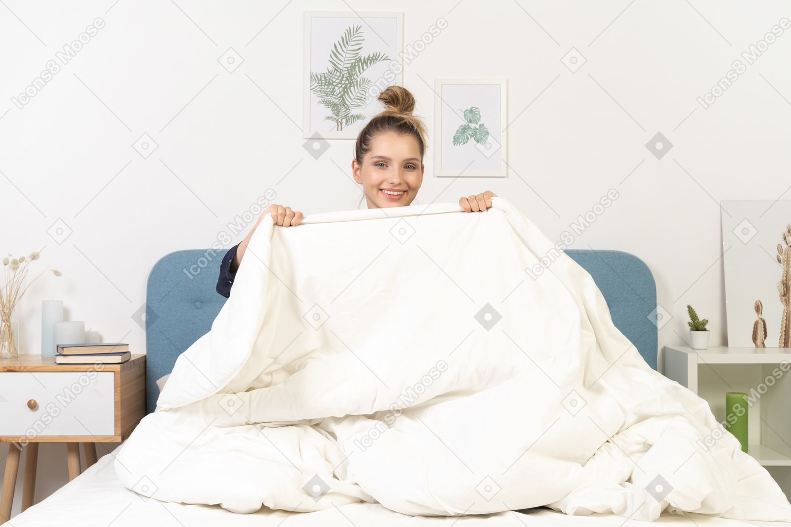 Front view of a smiling young woman in pajamas hiding behind the blanket staying in bed