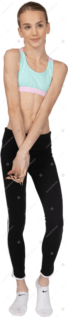 Vista frontale di una ragazza adolescente timida in abiti sportivi che tengono le mani insieme