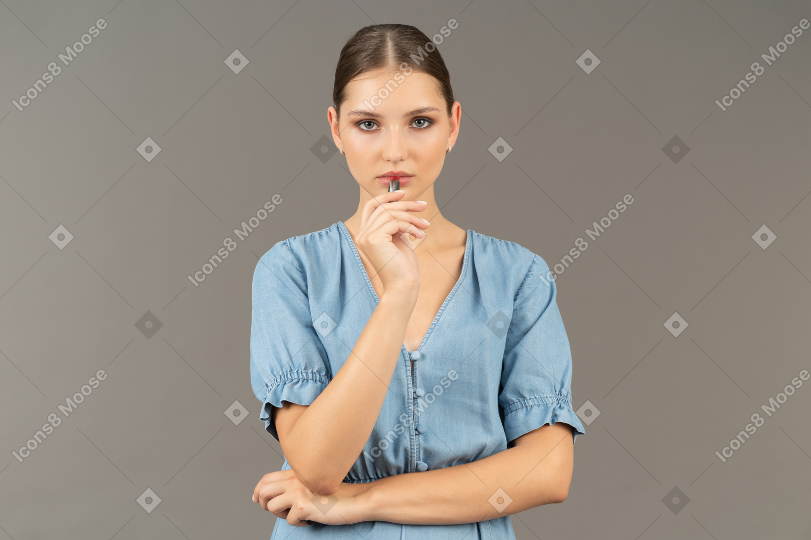Vue de face d'une jeune femme en robe bleue appliquant un rouge à lèvres