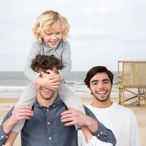 A man is holding a child on his shoulders at the beach