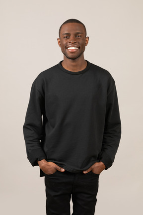 Vue de face d'un jeune homme souriant gardant les mains dans les poches