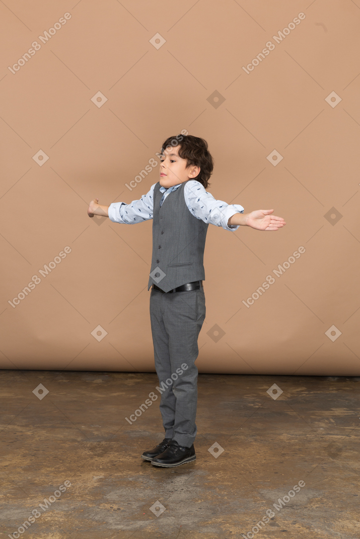 Side view of a boy in suit standing with outstretched arms