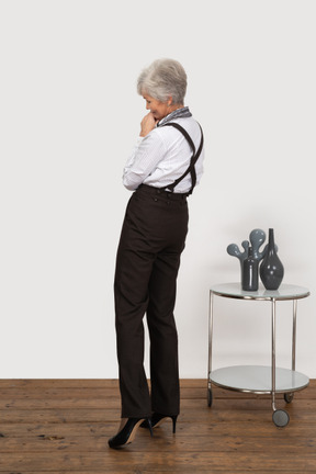 Dreiviertel-rückansicht einer erfreuten alten dame in bürokleidung, die hände zusammenhält