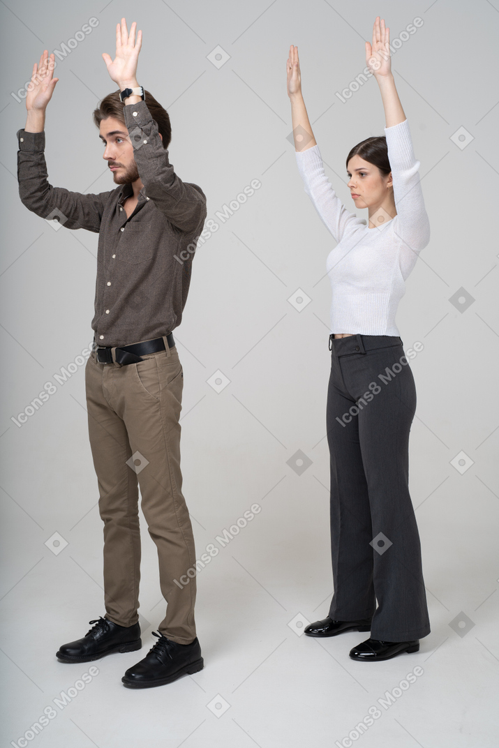 Vista de tres cuartos de una pareja joven en ropa de oficina levantando las manos