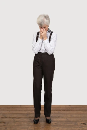 Front view of a worried old lady in office clothing holding hands together