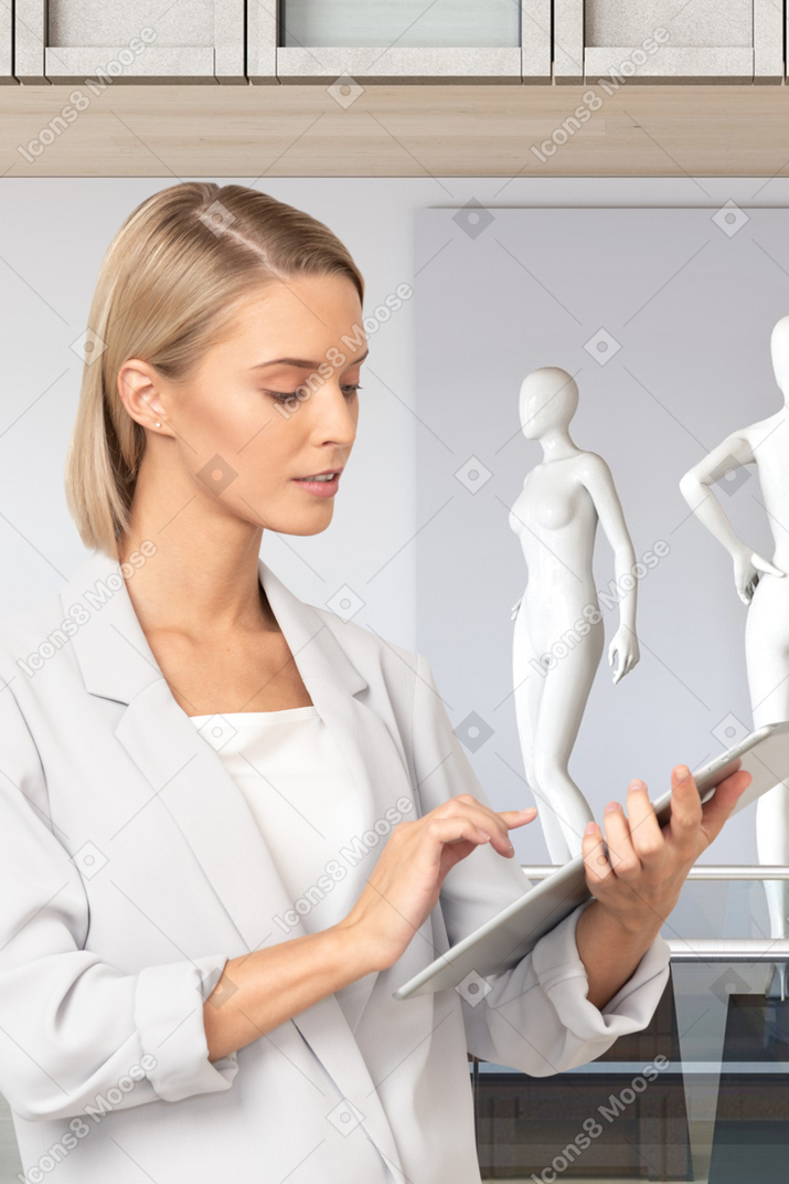 A woman is looking at a tablet while standing in front of mannequins
