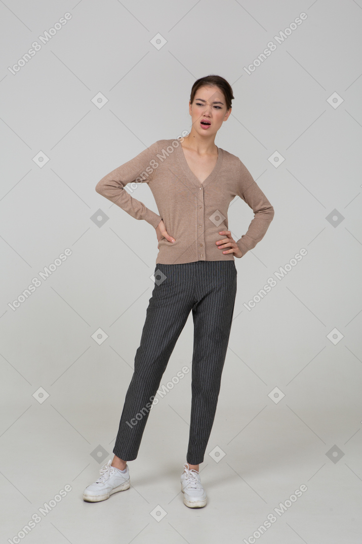 Front view of a suspicious young lady in beige pullover putting hands on hips
