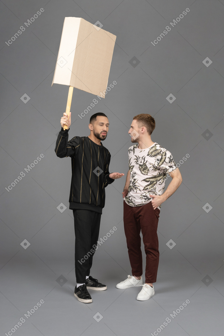 Junger mann mit einer plakatwand, der etwas mit einem anderen jungen mann bespricht