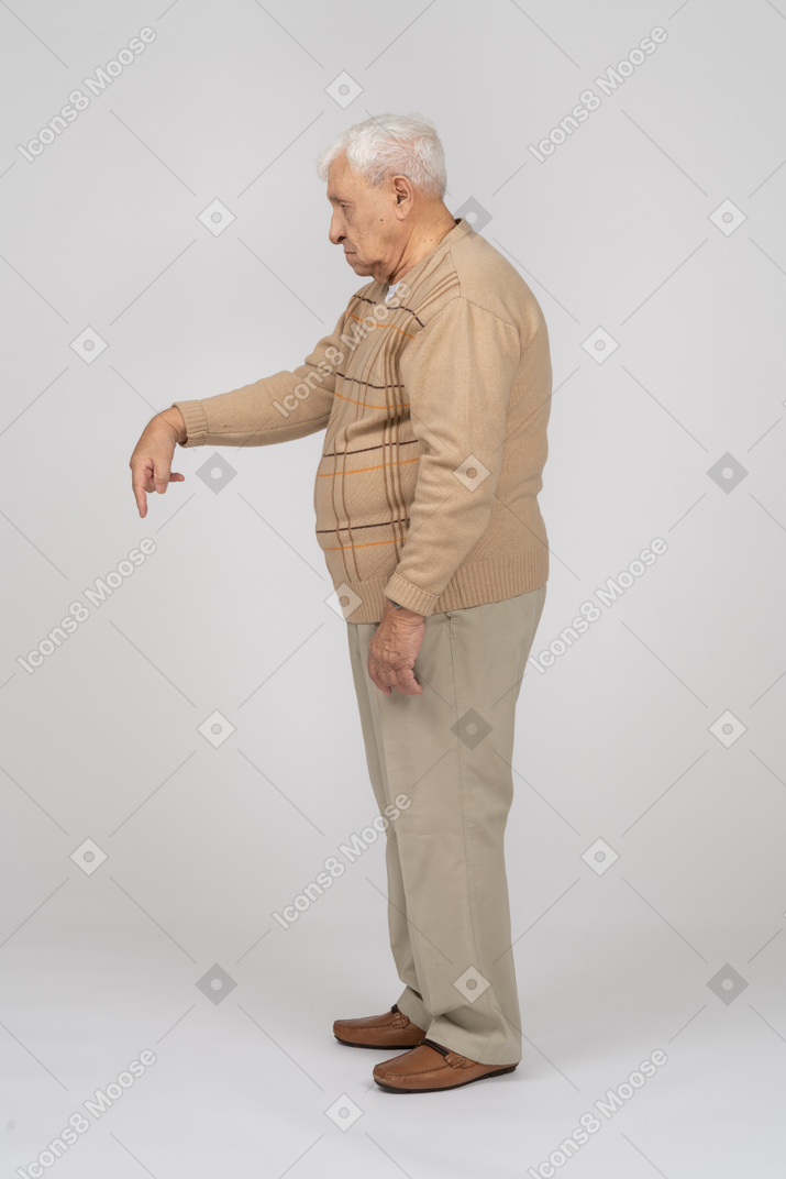 Vista lateral de un anciano con ropa informal apuntando hacia abajo con el dedo