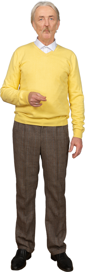 Front view of a puzzled old man in a yellow pullover raising hand and looking at camera