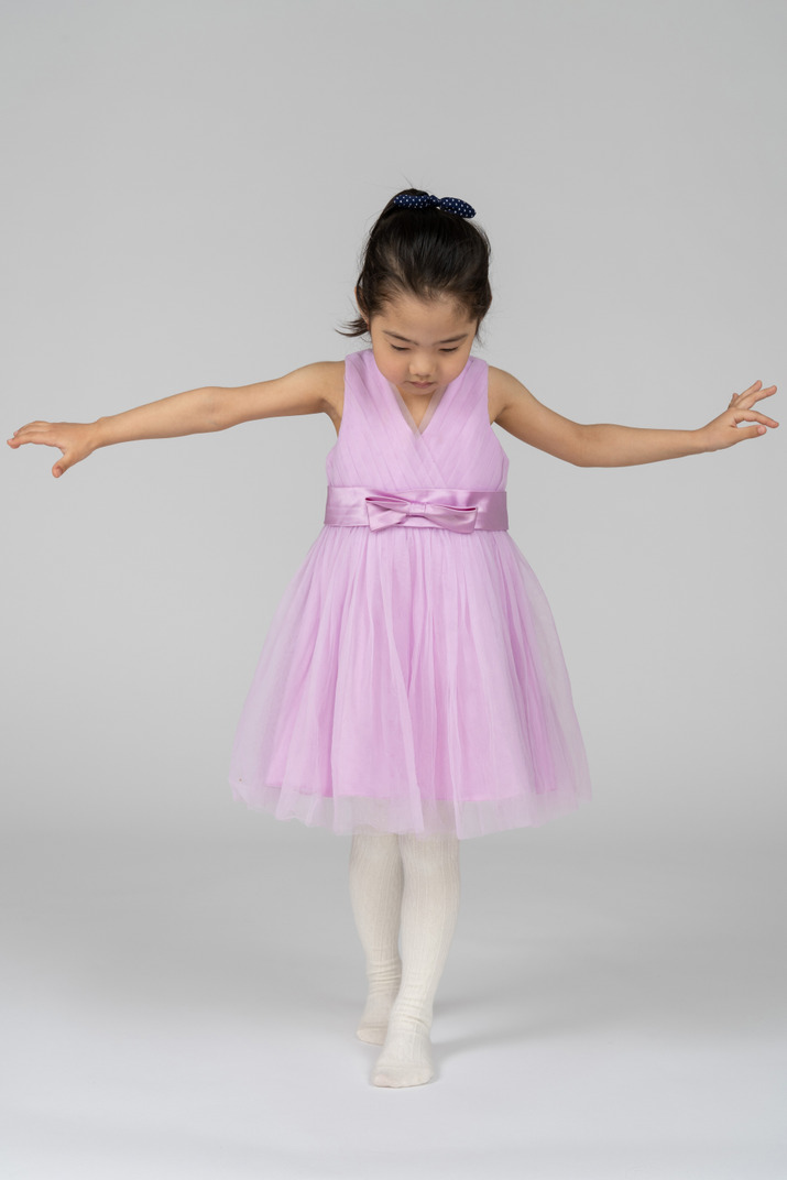 Girl in a pink dress keeping balance with spread arms