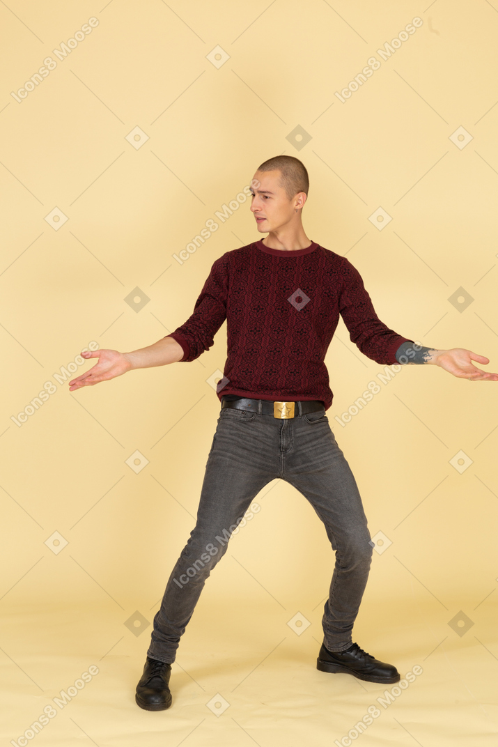 Vista frontale di un giovane uomo in pullover rosso in piedi con le gambe e le braccia diffuse