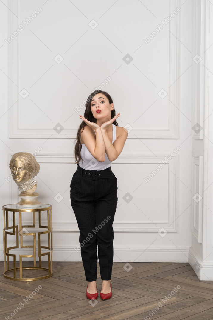 Front view of a cute young female leaning forward and sending air kiss near golden greek sculpture