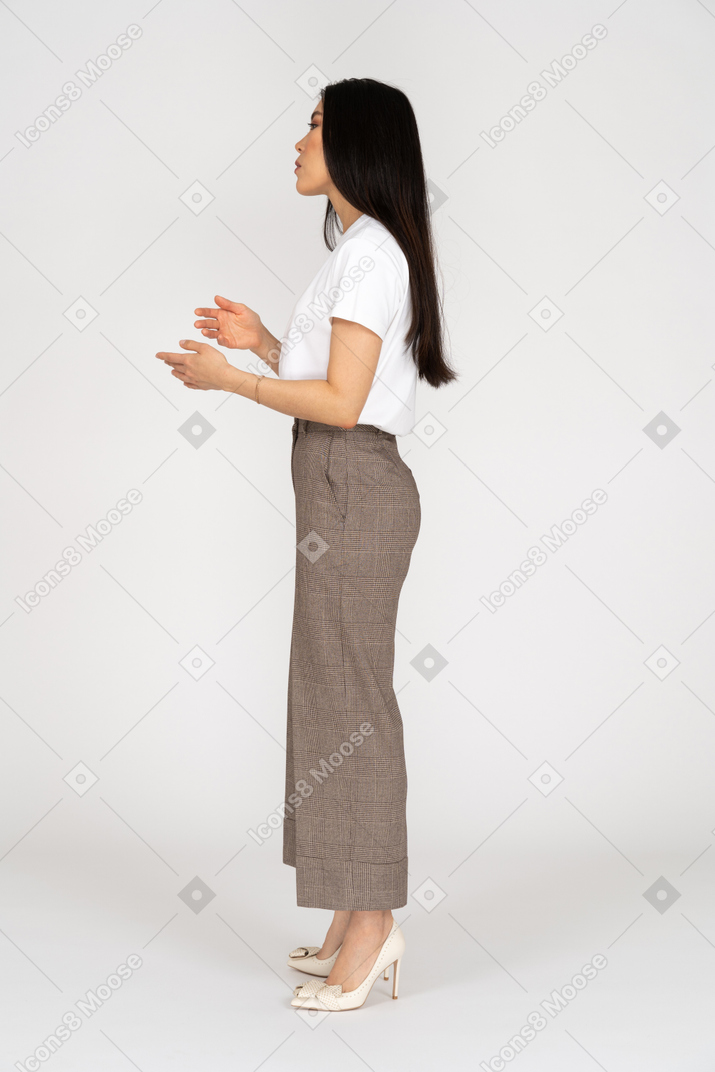 Vista lateral de uma jovem gesticulando de calça e camiseta explicando algo