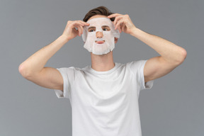 Front view of a young man putting on facial mask