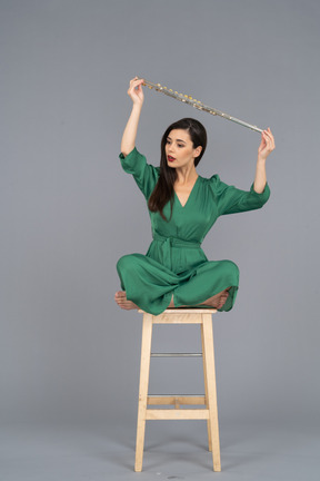 Pleine longueur d'une jeune femme tenant sa clarinette au-dessus de la tête alors qu'il était assis sur une chaise en bois