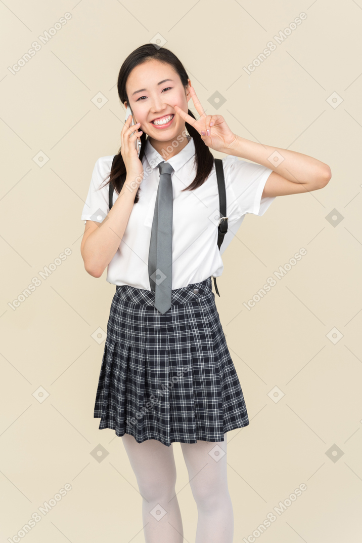 Asian school girl talking on the phone and showing v sign