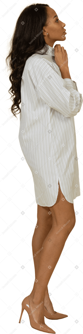 一位皮肤黝黑的年轻女性，穿着白色连衣裙，调整她的衣领的侧视图