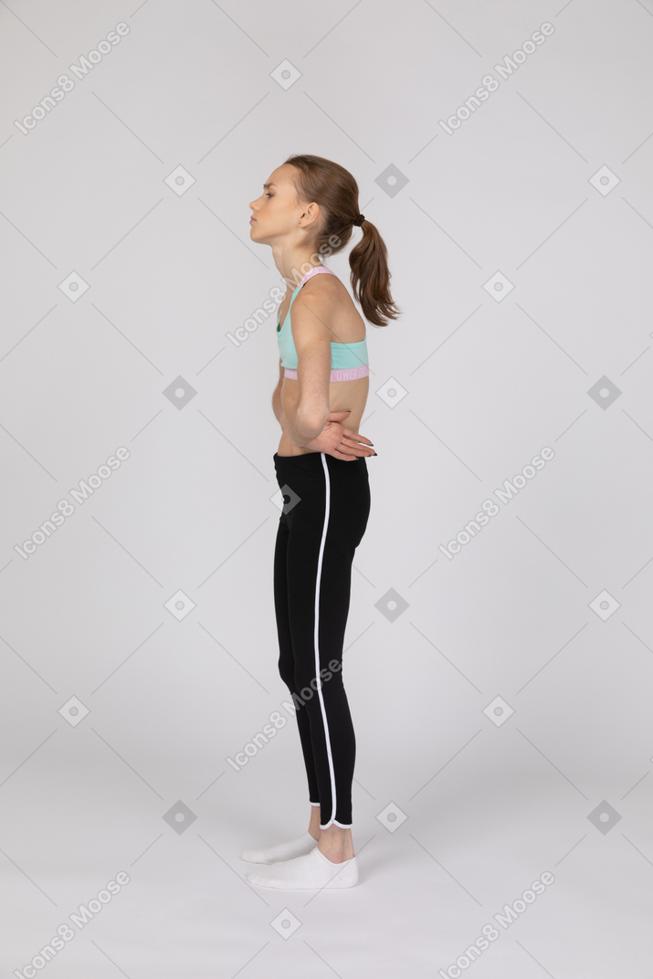 一个疲惫的青少年女孩，把手放在臀部上的运动服的侧视图