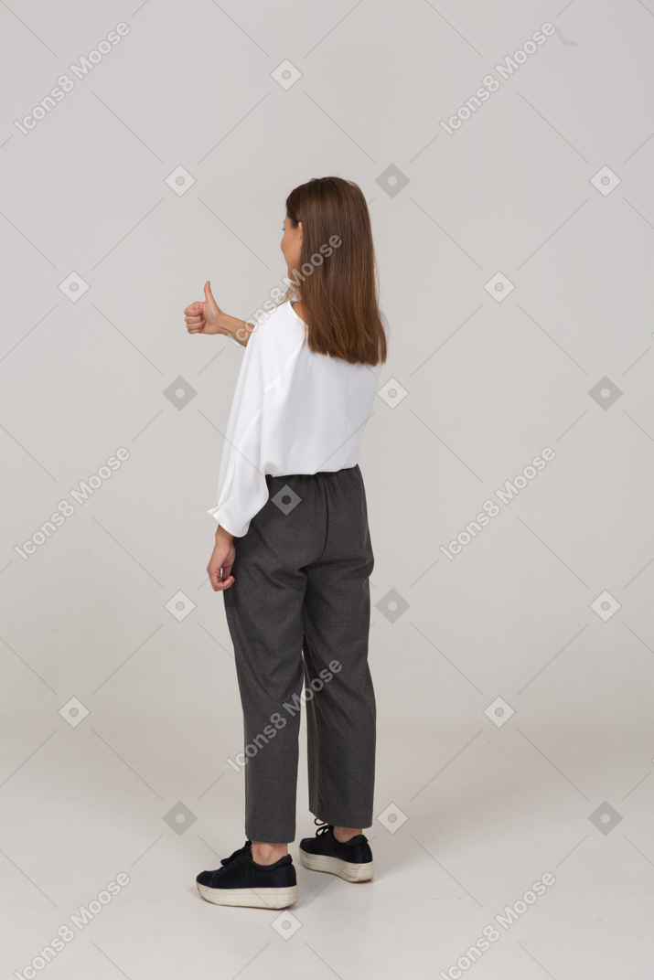 Вид сзади три четверти молодой леди в офисной одежде показывает палец вверх