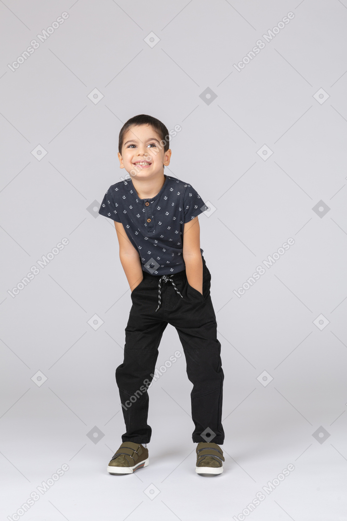 Front view of a happy boy in casual clothes posing with hands in pockets and looking at camera