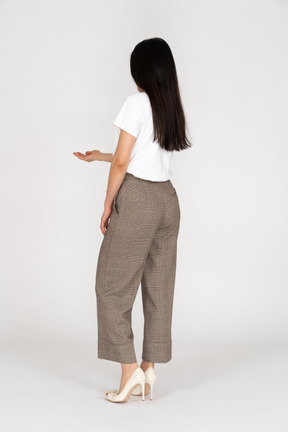 Vista posterior de tres cuartos de una joven en pantalones y camiseta extendiendo su mano