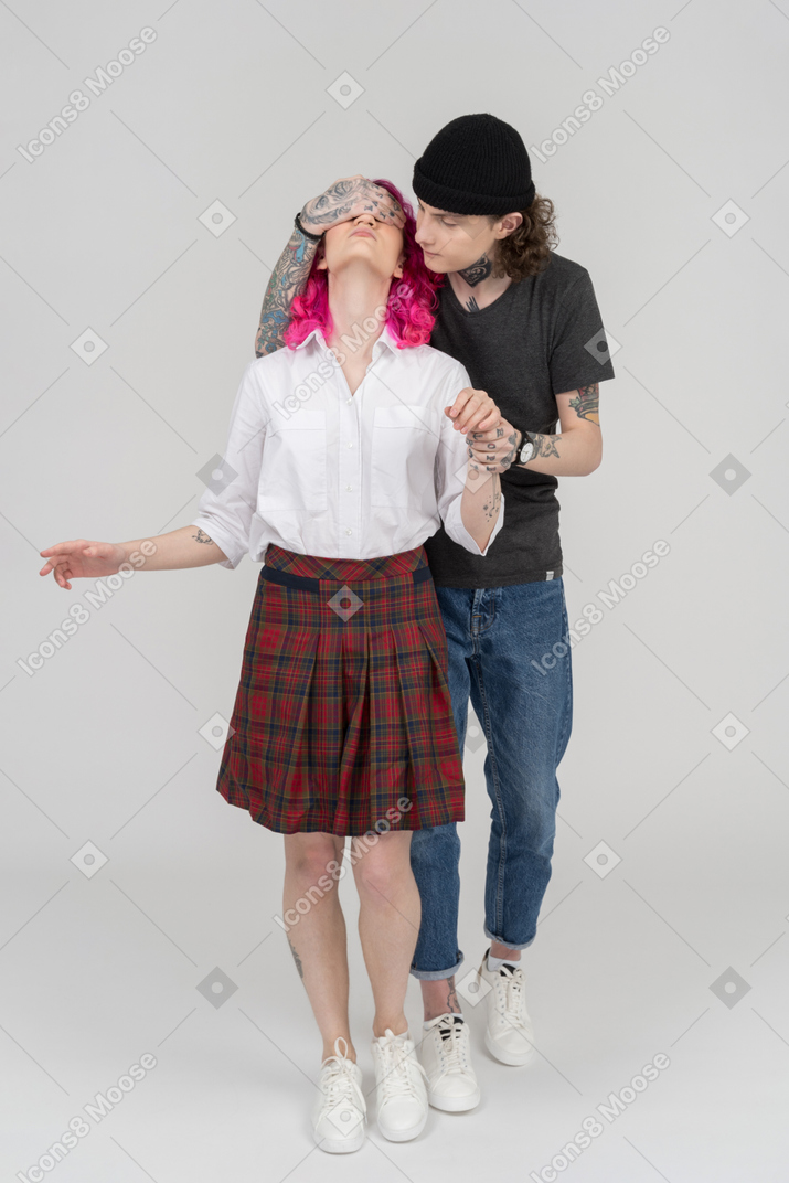 Young male standing behind his girlfriend shutting her eyes with an arm