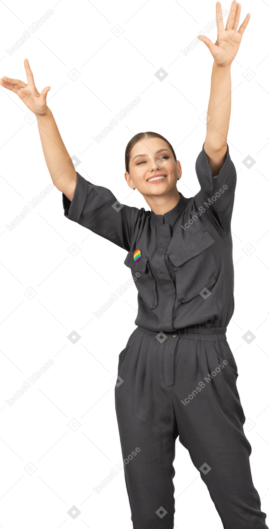 Front view of a young woman in a jumpsuit with lgbt pin raising hands
