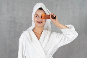 Woman in bathrobe smiling while holding tube over eye