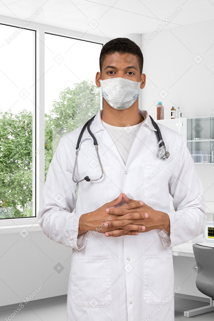 A male doctor wearing a mask and holding his hands together