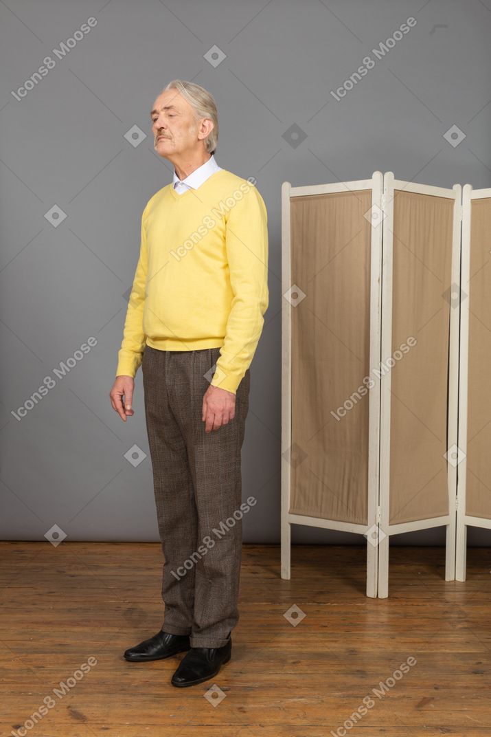 Вид в три четверти грустного старика, стоящего на месте и смотрящего вниз